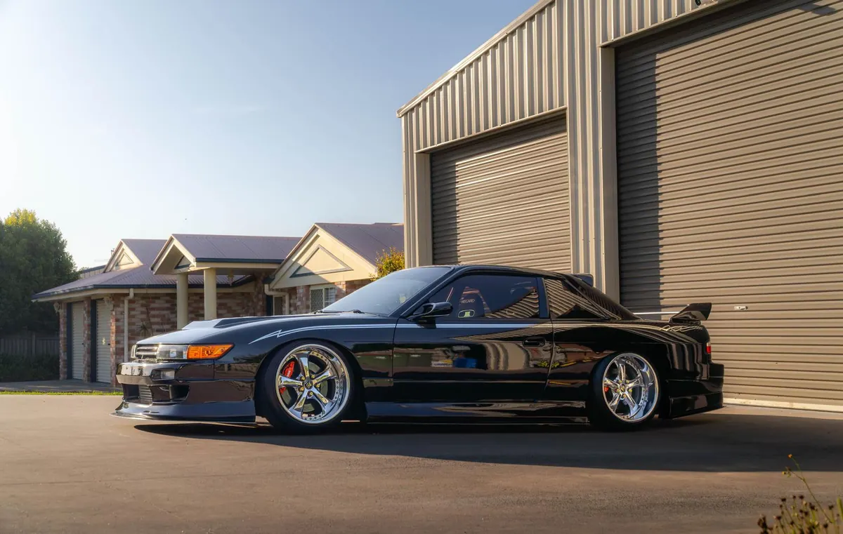 Black Nissan Silvia S13 with polished paintwork beside a shed at golden hour